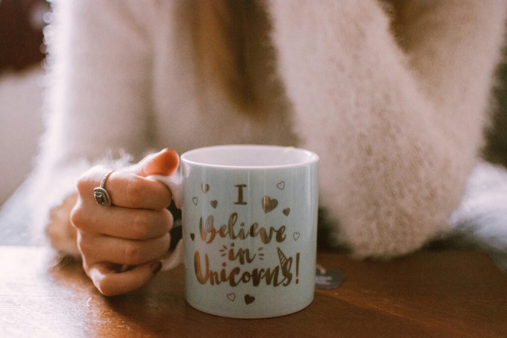 Hand holding a unicorn-themed mug with a cozy and warm vibe, perfect for morning coffee or tea.